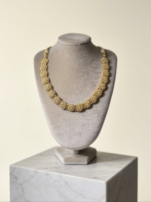 Gold necklace on a gray bust against a beige background